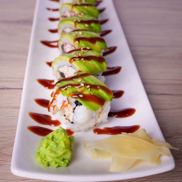 Hornbill Sushi & Asian Fusion's avocado-topped sushi rolls with sauce, wasabi, and ginger on a white plate.