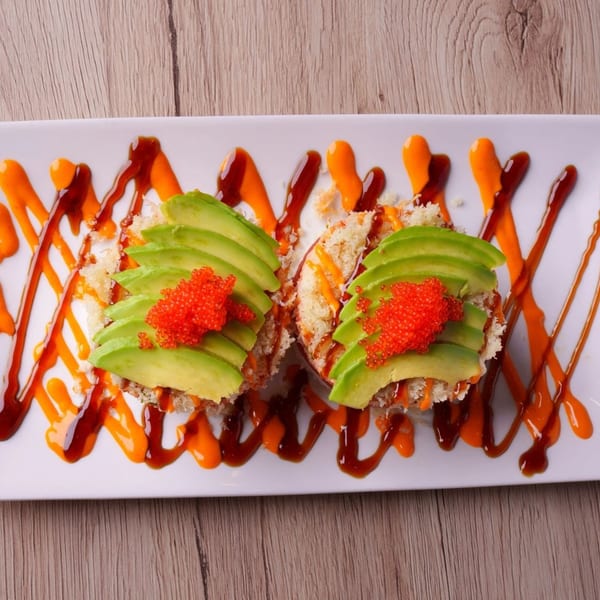 Two Hornbill Sushi rolls topped with avocado slices and bright red tobiko, drizzled with sauces.