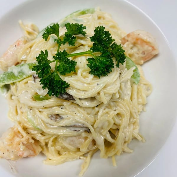 Creamy pasta with shrimp, green beans, mushrooms, and parsley on a white plate.