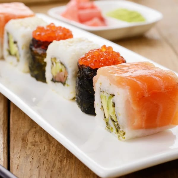 A white plate holds a row of Hornbill Sushi rolls, some topped with salmon and roe.