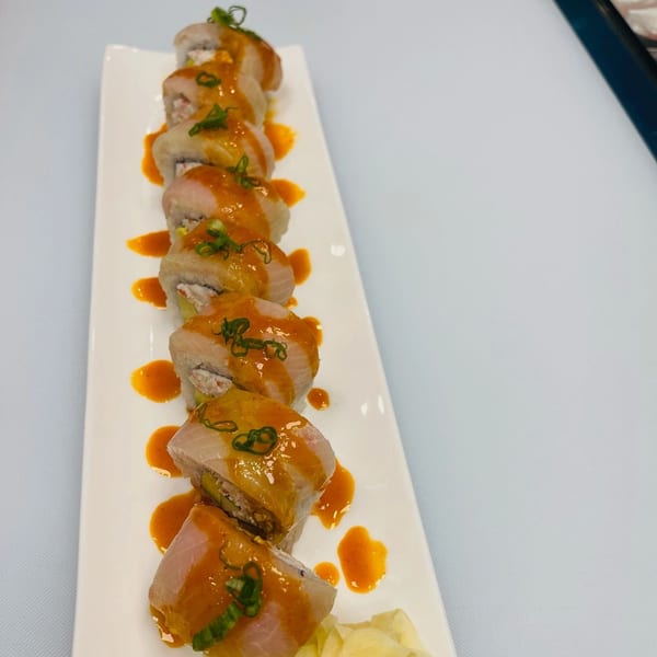 Hornbill Sushi's Asian fusion sushi roll, topped with orange sauce and green onions, on a white plate.