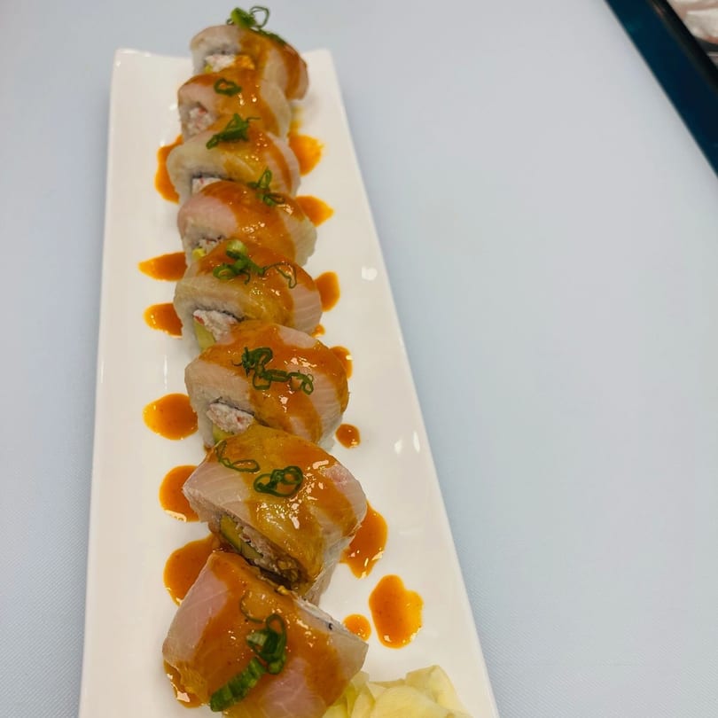 Hornbill Sushi's Asian fusion sushi roll, topped with orange sauce and green onions, on a white plate.