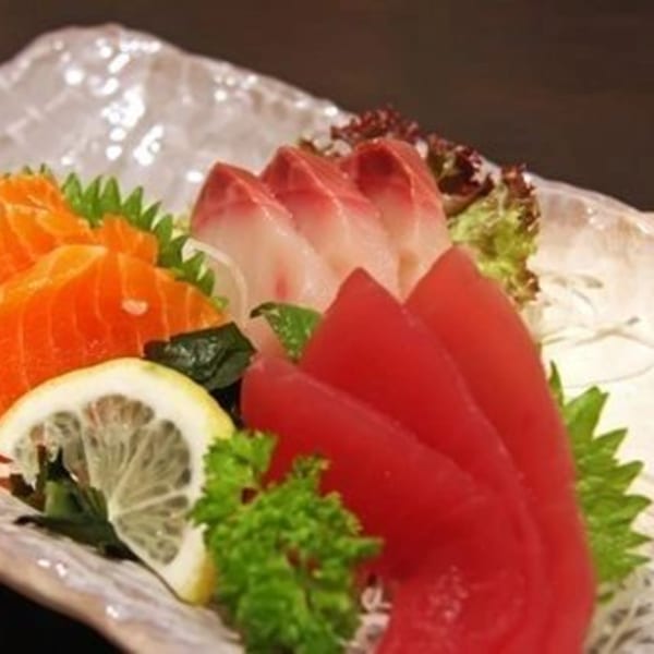 Assortment of fresh sashimi, including salmon, tuna, and white fish, garnished with lemon and greens.