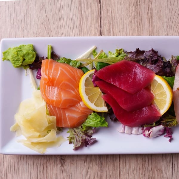 Sashimi platter with salmon, tuna, lemon, ginger, wasabi, and mixed greens on a white plate.