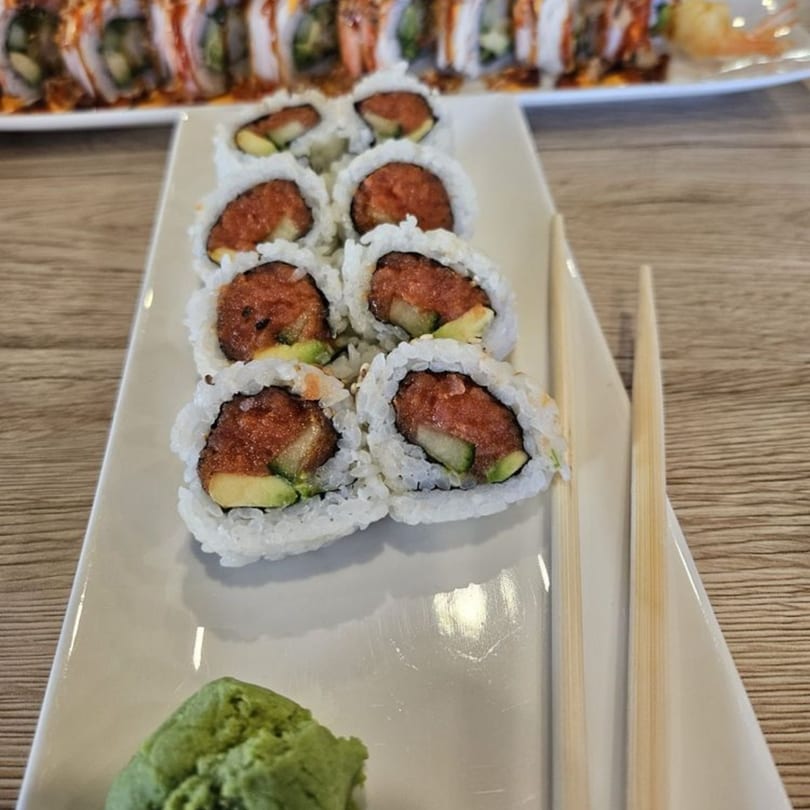Hornbill Sushi's spicy tuna and avocado sushi rolls with wasabi and chopsticks on a white plate.