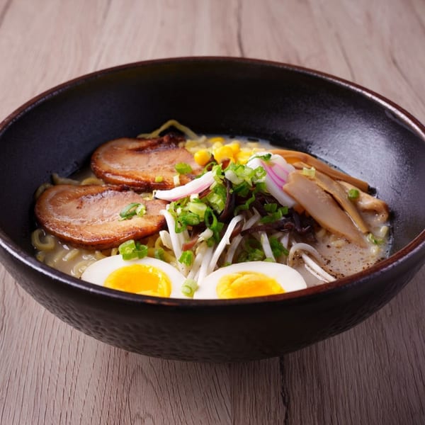Hornbill Sushi & Asian Fusion ramen with pork, egg, corn, and vegetables in a black bowl.