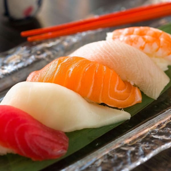 Assorted Hornbill Sushi nigiri, including tuna, salmon, white fish, and shrimp, with red chopsticks.