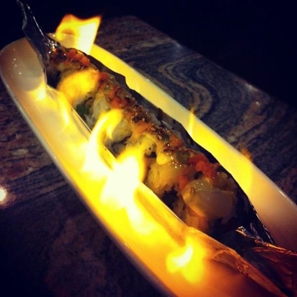 Flaming Hornbill Sushi roll, topped with sauce and sesame seeds, served on a white dish.